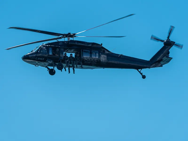 Black military helicopter in flight with rotor blades frozen mid-spin