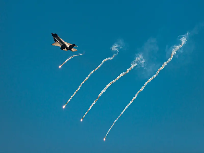 F-35A banking away while trailing curved white flare smoke streams across the sky