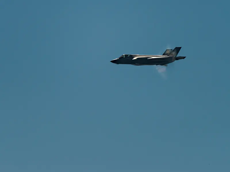 Side profile of an F-35A jet flying past with a faint vapour halo