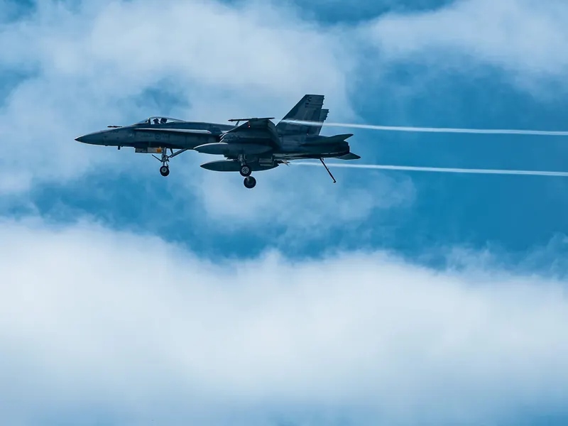 CF-18 Hornet fighter jet with vapour trails flying in front of bright white clouds