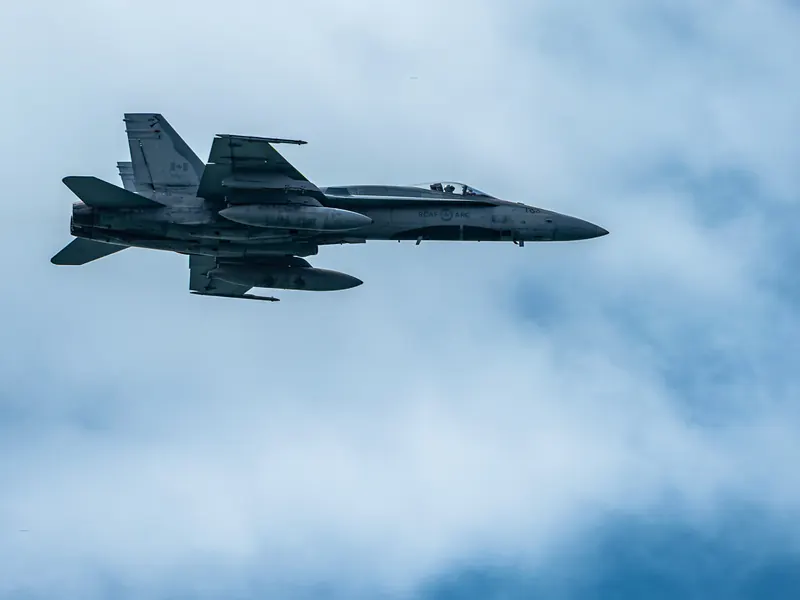 Fighter jet flying left to right past soft cumulus clouds