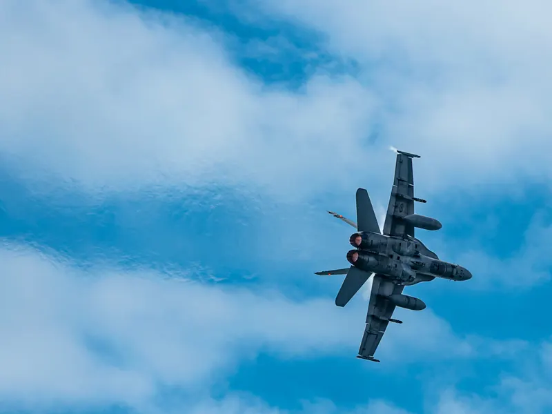 Fighter jet banking to show its topside against blue sky and scattered clouds