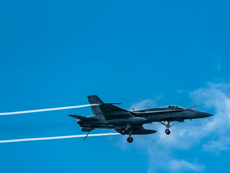 Fighter jet with landing gear down and white vapour trails streaming behind