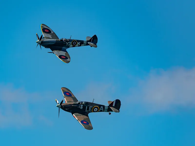 Two vintage camouflaged warbird fighters flying together in a blue sky