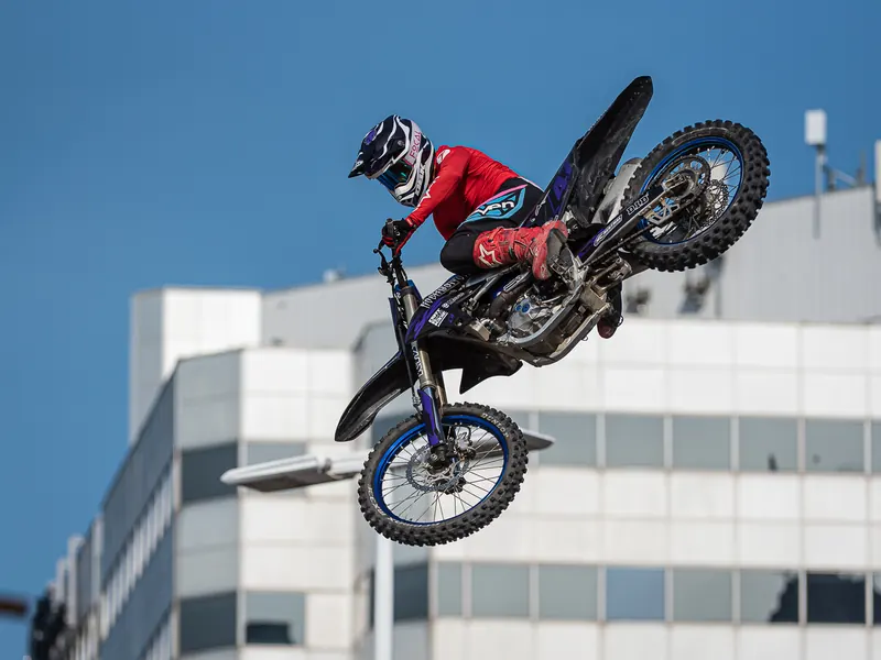 Motocross rider in red airborne over the rooftops during a freestyle jump