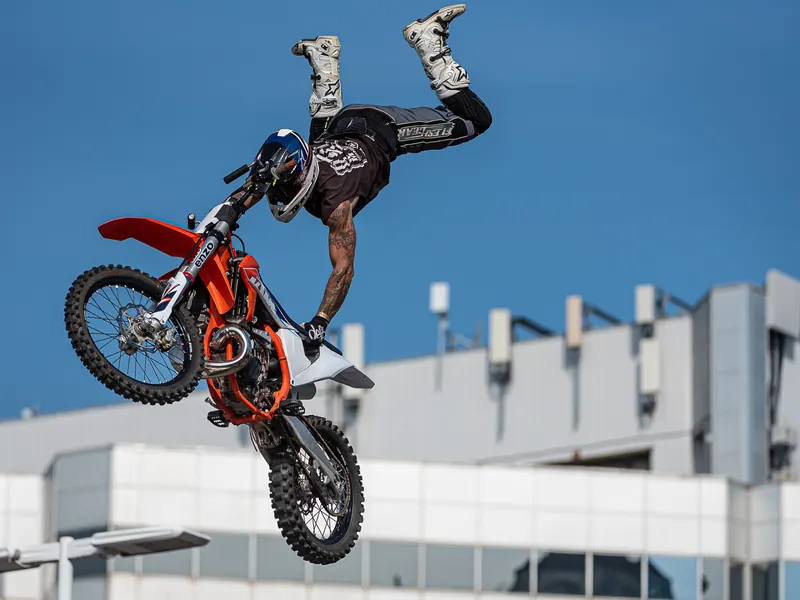 Freestyle motocross rider stretched behind an orange dirt bike in mid-air