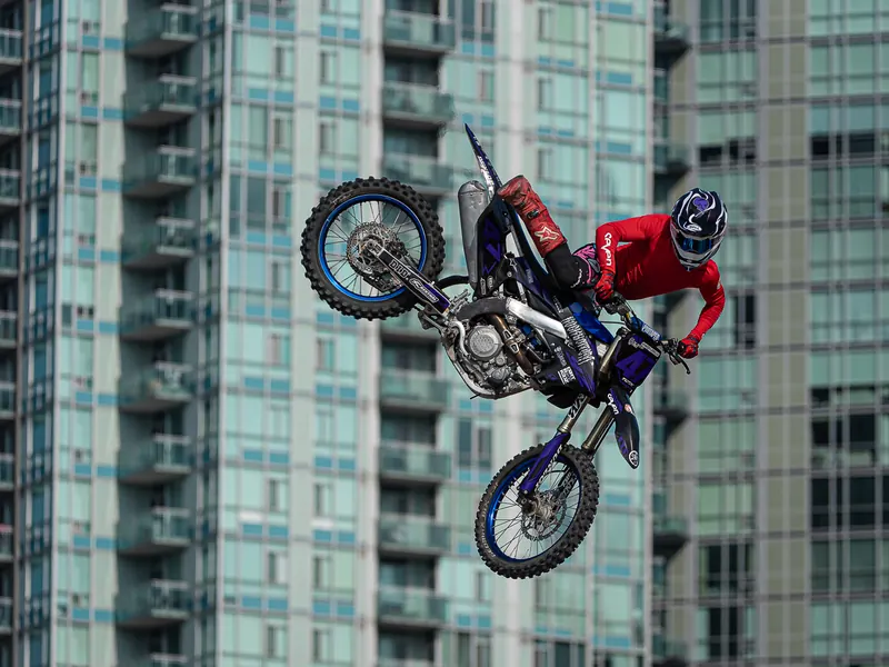 Freestyle motocross rider in mid-air framed against a glass residential tower