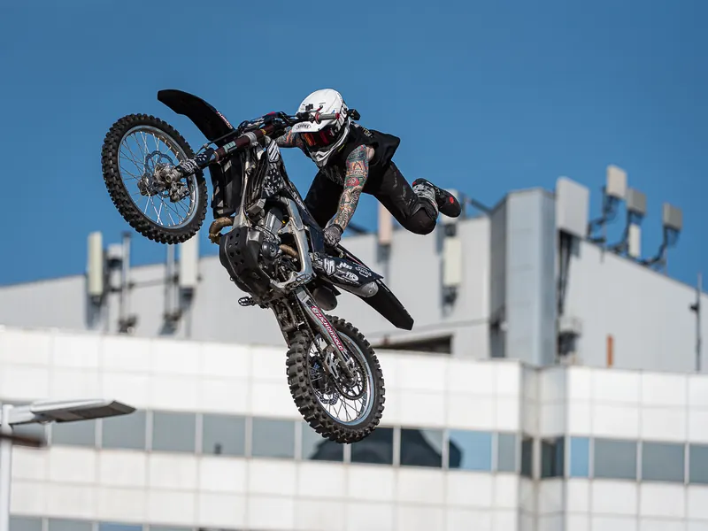 Freestyle motocross rider fully extended above the bike mid-air against city buildings