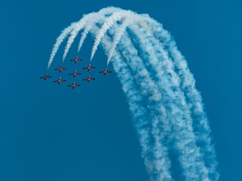 Snowbirds formation team pulling a sweeping arc of white smoke trails across a deep blue sky