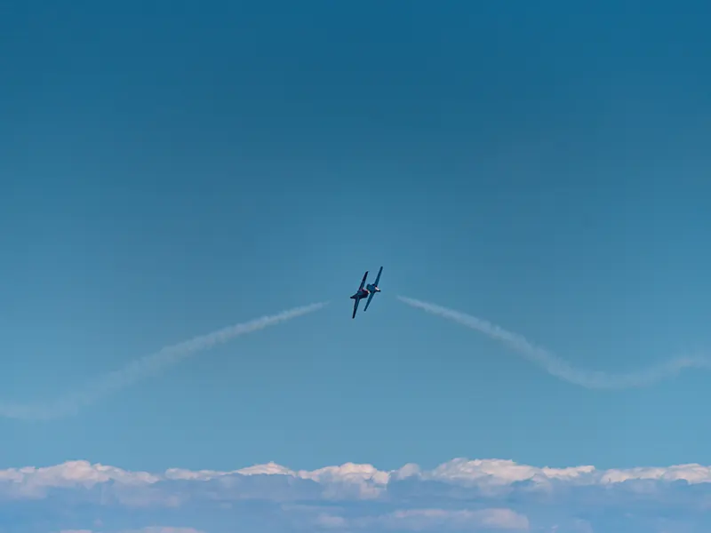 Jet flying low over a distant horizon of clouds, trailing a thin smoke line