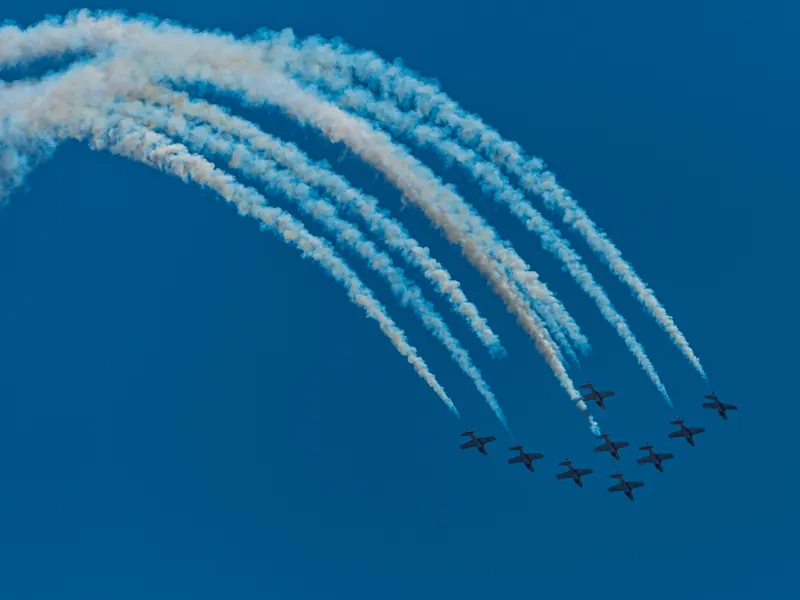 Nine-jet Snowbirds formation at the bottom of a loop, smoke trails curving overhead