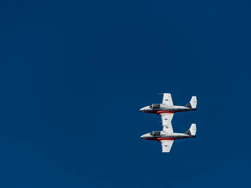 Two red and white Snowbirds jets flying in a stacked mirror formation