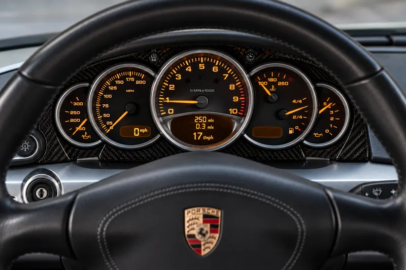 Close-up of an orange-lit analogue instrument cluster behind a steering wheel