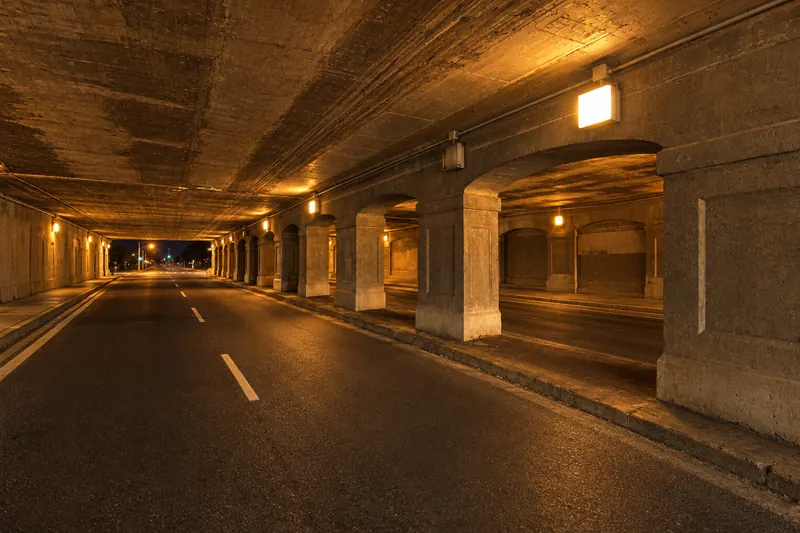 Empty concrete tunnel lit by rows of warm amber lamps, used as a background plate