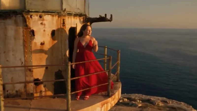 Woman in a red gown at a clifftop lighthouse above the sea at golden hour — thumbnail for the Parasonisi lighthouse video